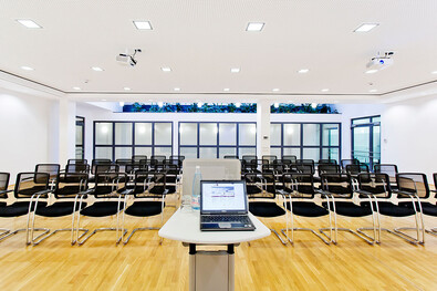 Foto des geräumigen und offenen Konferenzraums im Atrium mit Kinobestuhlung für ca. 90 Personen aus der Perspektive des Redners..