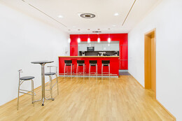 Barraum im Erdgeschoss, rote Bar und freistehender Bartisch mit Barhockern